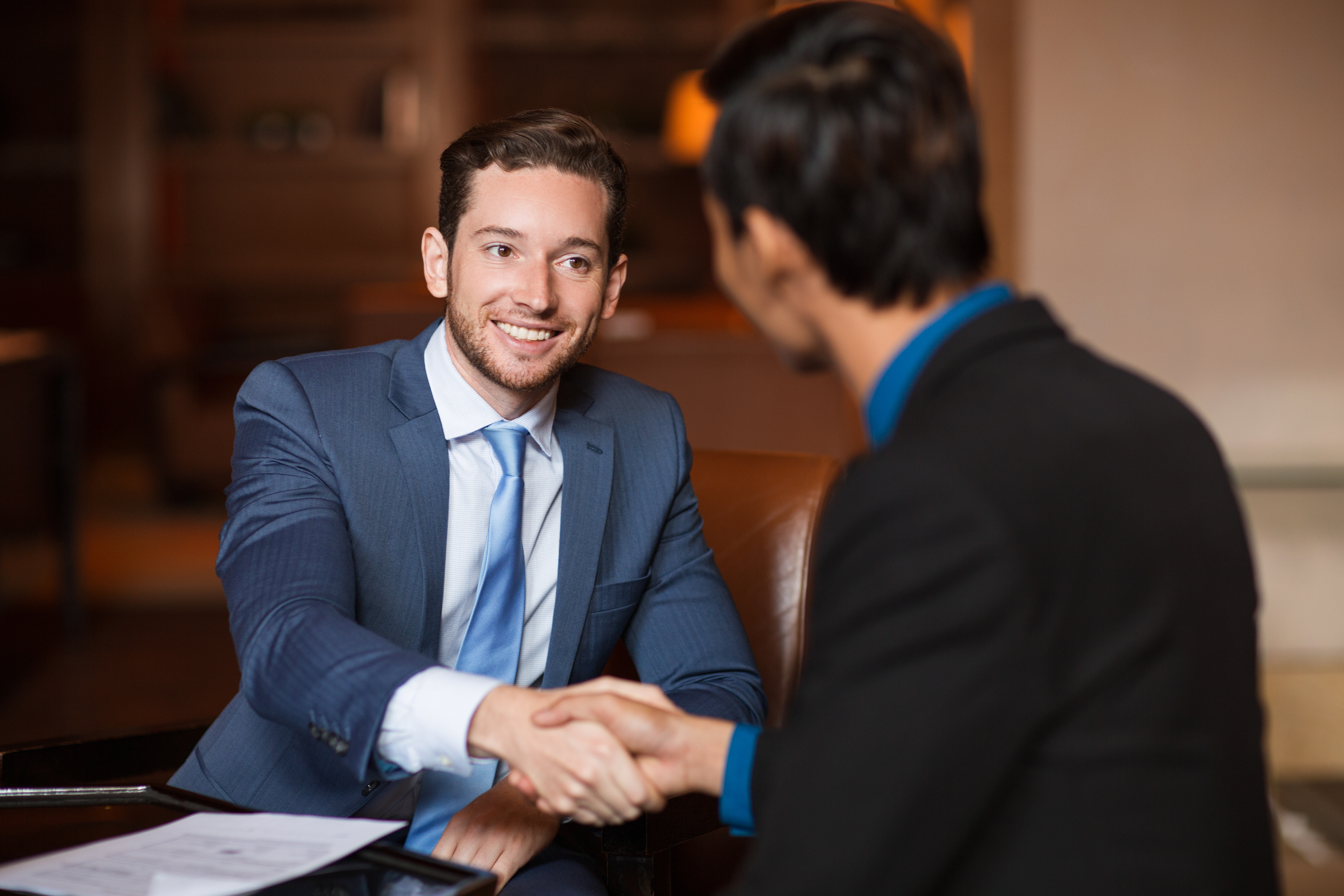 Closeup of two smiling business men shaking hands in cafe. One man is sitting back to camera.